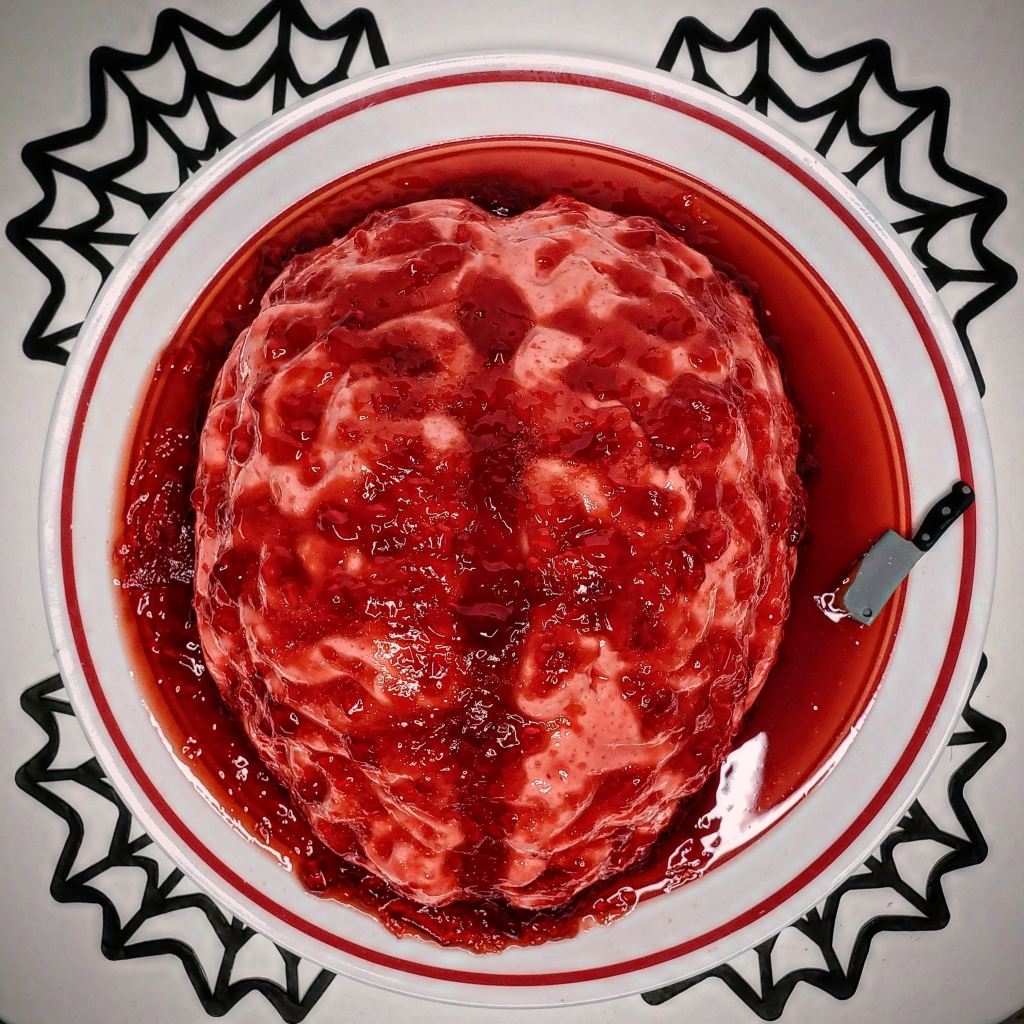 A opaque pink gelatin dessert in the shape of a brain, with red, globby gelatin poured over top to simulate blood.